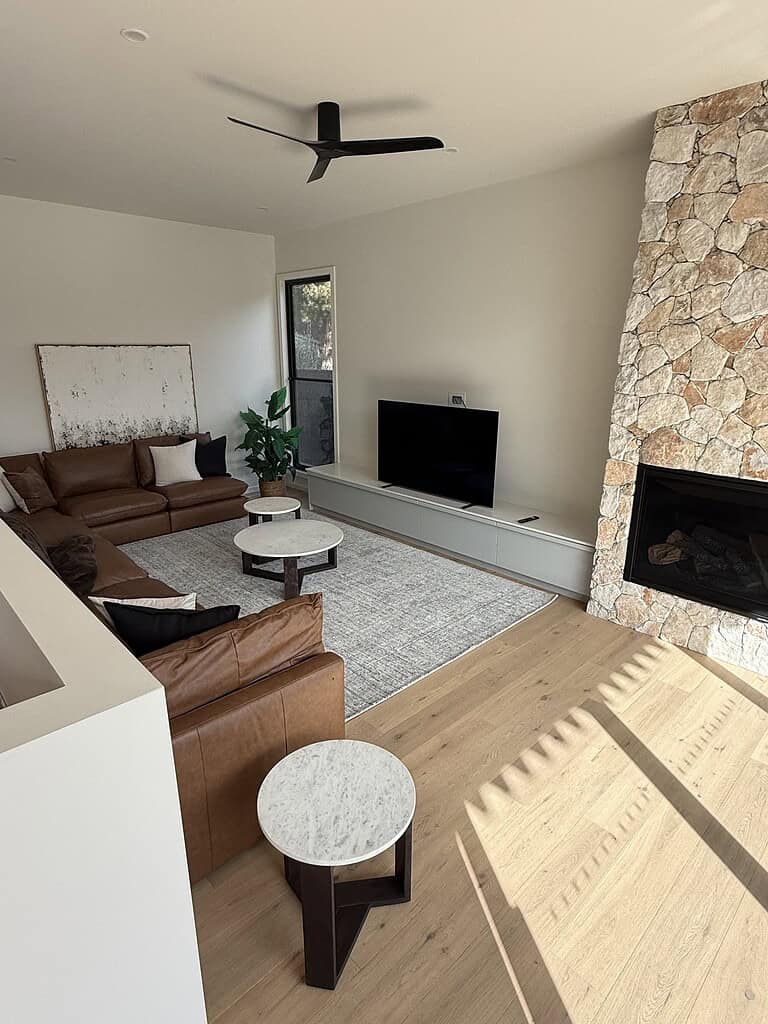 Bright living room featuring leather couches, a stone fireplace, and a flat-screen TV under natural daylight.