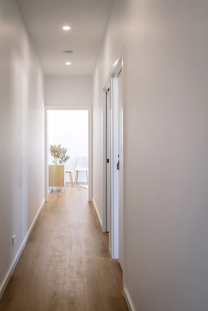 Bright hallway with wooden flooring, white walls, and modern recessed ceiling lights.